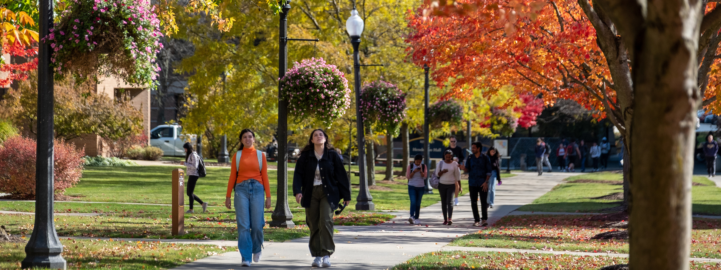 Students walk across campus, surrounded by trees with leaves in a variety of fall colors