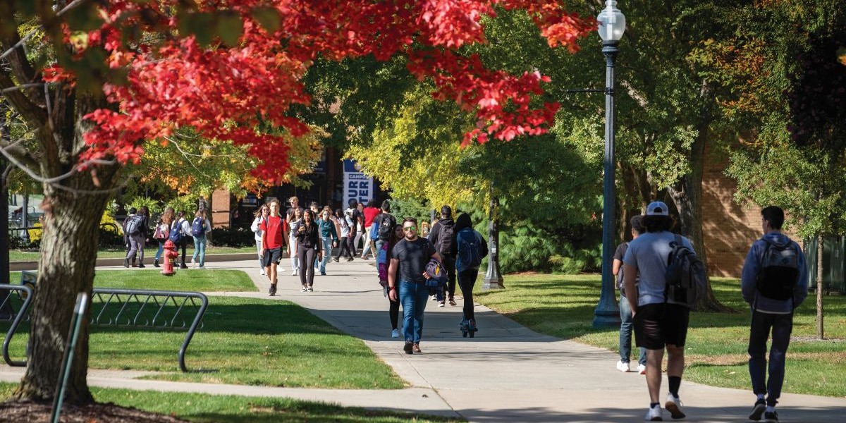 Students walk across campus, surrounded by trees with leaves in a variety of fall colors